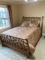 Full view of full size metal sleigh bed with floral bedding and pillows in bedroom near window.