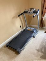 Full view of Nautilus treadmill indoor on carpet in a room with beige walls and curtains.
