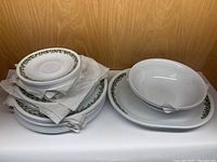 Stack of large, medium, and small plates with two bowls and two platters showing green floral border on white Corelle dinnerware.