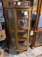 Front view of the oak curved glass display cabinet showing its key lock front door and wood shelves inside.