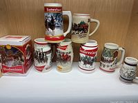 Front view of 8 Budweiser steins in varying sizes with winter and holiday themed artwork featuring Clydesdale horses.