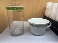 Glass tumbler next to a matching Corelle coffee/tea cup showing the green floral grapevine pattern.