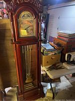 Full view of the tall wooden grandfather clock showing carved details, pendulum, and weights inside glass door.