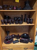 Front view of shelving unit displaying ruby red glassware including goblets, cups, candle holders, plates, and serving dishes.