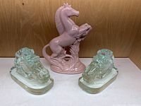 Front view of all three horse figurines including the pink rearing horse in the center and clear glass horse head bookends on either side.