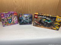 Three unopened Lego sets displayed side by side: LEGO Friends, Marvel Eternals, Creator Monster Truck.