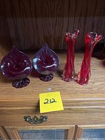 Full view of the four red glass items: two leaf-shaped vases (left) and two tall swirled candle holders (right).