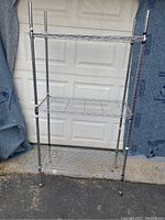 Full view of metal wire rack cart with three shelves and four vertical poles on caster wheels. Missing plastic shelf liners on shelves.