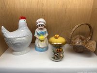 Four ceramic pieces on display including chicken container, chef figurine, mushroom jar, and basket container