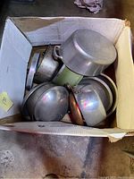 Top view of box filled with different vintage cooking pots, showing aluminum and copper materials.