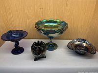Four carnival glass pieces arranged in a row on table against wood background, showing different shapes and colors.