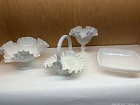 Full lot of four milk glass pieces displayed on a white cloth with wood background.