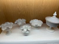 Five-piece milk glass set with silver lace ruffled edges includes three pedestal bowls, one covered pedestal compote, and one small ruffled bowl, all white opaque milk glass.