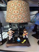 Full view of the vintage nursery lamp showing the patterned lampshade, wooden base, girl figurine in rocking chair, and cat figurine on base.