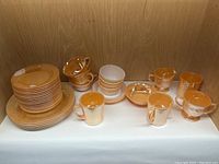 Full view of all glassware arranged showing plates, cups, bowls and mugs with peach luster finish and white bowls.