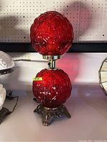 Full side view of the vintage red glass table lamp showing both upper and lower glass globes attached to the metal base.