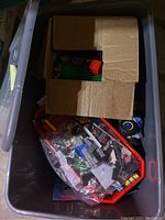 Open tote with loose LEGO pieces in plastic bags, a red tray, and a cardboard box inside the bin.