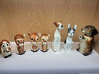 Seven ceramic dog figurines lined up, including one dog shaped as a pitcher.