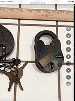 Close up photo of two antique padlocks and associated keys on white tile with ruler for scale