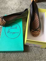 Black flat shoes with leopard print toe caps placed beside Jack Rogers boxes.