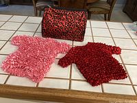 Photo showing pink and red expandable bubble tops and the red and black leopard travel bag on a grid-tiled table