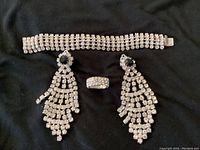 Vintage jewelry set featuring large clear stone earrings with black centers, thick clear stone bracelet, and clear stone ring displayed on black fabric.