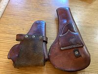 Close-up of the smaller, plain leather holster with visible snap strap and stitching.