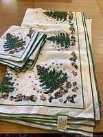 Folded tablecloth and six folded napkins showing Christmas trees and gift patterns with green border