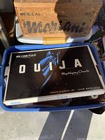 Photo of a vintage William Fuld Ouija board set box with distinctive black and white design showing a robed figure and text.