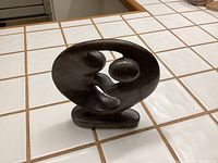 Side view of the dark stone sculpture showing the two abstract figures dancing within an oval frame on a base