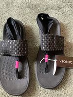 Photo showing pair of black Vionic sandals with metallic woven upper band and toe post with pink accents, with tags attached.