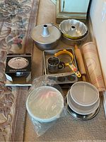 Overview of bakeware assortment with steamer, cake pans, cupcake tin, rolling pin, sifters, mixing bowls, and pastry mat.