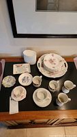 Overview of cups, saucers, plates including floral patterns and some small decorative plates.