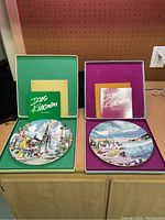 Two Dong Kingman collector plates displayed in their original cases, one case green and the other purple, each with signed collector information booklet.