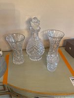 Full set of four cut glass pieces displayed on a surface against wall: one wine decanter with stopper, two vases, one sugar bowl with lid.