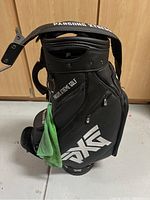 Front side view of the black Parsons Xtreme Golf carry bag showing PXG logos and a green towel attached.