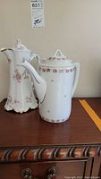 Two porcelain pitchers or teapots by Haviland and Company on wooden surface, showing front and side views.