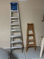 Photo showing both aluminum 8-foot ladder with blue paint shelf and 5-foot wooden ladder folded, side by side.