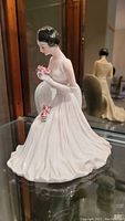 Photo of the seated female porcelain statue holding pink flowers, showing detailed features and dress.