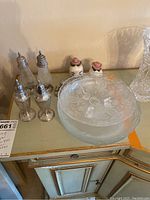 Three sets of salt and pepper shakers, sterling silver with metal tops and one porcelain set, four clear etched glass plates, and a raised glass candy dish.