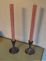 Pair of weighted sterling silver candlestick holders with pink textured candles standing on a table, casting shadows on wall