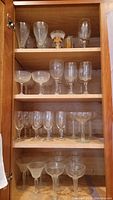 Full cabinet shelf with assorted stemware glasses including tall wine glasses, coupe glasses, and decorated glasses.
