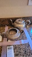 Silver soldered interior teapot with lid and curved spout, placed on a granite countertop.