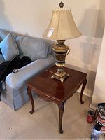 Photo showing the wooden end table with carved legs and polished top, with the lamp placed on it beside a sofa.