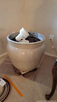 Full view of the large beige terracotta pot filled with soil, sitting on a wheeled base, with the spot lamp inside it.