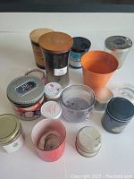 Photo showing 13 assorted empty candle jars of various materials and sizes arranged on a white surface.