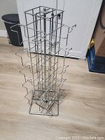 Metal wire rotating card stand with multiple slots on a light wood floor, showing its full height and structure.