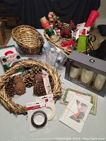 Photo of entire lot with LED candle set in box, sleigh baskets filled with various craft materials, pine cones, ribbons, and Christmas cards laid out on table.