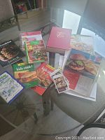 Photo showing the assortment of cookbooks, recipe booklets, spiral notebooks and recipe cards spread on a glass table