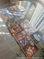 Photo showing 12 DVDs laid out on a glass table, including Star Wars Trilogy and other various movie titles.